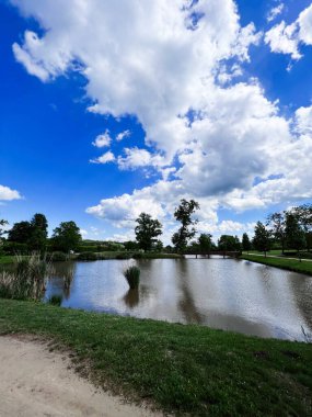 Bu sakin manzara, Çek Cumhuriyeti 'nin Kunstat kentindeki tüylü bulutlarla kaplı canlı mavi gökyüzünü yansıtan huzurlu bir gölet yakalıyor..