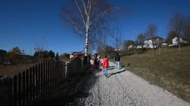 Kırsal kesimde bir sonbahar gününde çakıl yolda yürüyen bir aile. Resimli yol boyunca birlikte dolaşırlar. Güneşli bir günde güzel mavi gökyüzü ve gölgelerle çekilen.