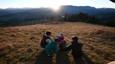 Aile gün batımında dağlarda kamp ateşi yakıyor. Ateşin sıcak parıltısı, hikayelerini ve kahkahalarını paylaşan samimi bir atmosfer yaratıyor. Nefes kesici dağ manzarası.