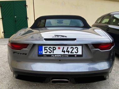 Brno, Çek Cumhuriyeti - 15 Nisan 2022: Yeşil bir kapının yanına park edilmiş siyah yumuşak bir üstü açık, modern gümüş renkli üstü açık bir Jaguar F tipi araba.. 