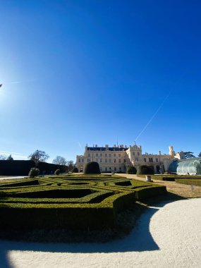 Büyük bir Lednice şatosunun çarpıcı manzarası titizlikle budanmış çalılar ve parlak mavi gökyüzü ile çevrili, mimari güzellik ve sükuneti gözler önüne seriyor, Çek Cumhuriyeti.