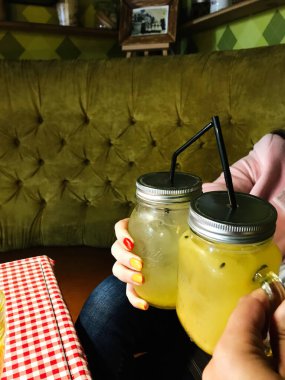 İki kişi, hoş, eski moda bir ortamda serinletici sarı içeceklerle dolu mason kavanozlarını tıkıyor. Renkli tırnakları gündelik atmosfere eğlenceli bir dokunuş katıyor..