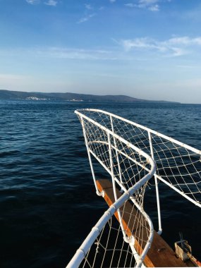 Bir kayığın korkuluğu, berrak mavi bir gökyüzünün altında uzanan sakin okyanusun üzerine uzanır, dingin ve geniş bir deniz manzarası yakalar..