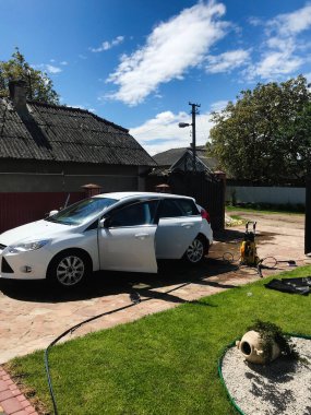 Bereketli yeşilliklerle çevrili ve parlak mavi bir gökyüzünün altında beyaz bir araba konut yolunda temizleniyor. Sahne temizlik, bakım ve banliyö yaşamını taşır.