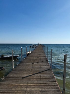Huzurlu mavi bir okyanusa uzanan uzun, ahşap bir iskeleden oluşan huzurlu bir sahne. Açık gökyüzü ufkun dinginliğini ve sonsuz hissini arttırır..