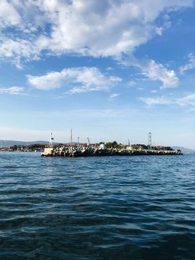 Sakin bir sahil sahnesinde berrak mavi gökyüzünün altında sakin dalgalar var. Küçük bir liman ve pitoresk bir manzara huzur ve sükunet için mükemmel sakin bir atmosfer sunar..