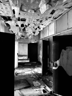 Harap olmuş bir koridorun tek renkli görüntüsü dağınık döküntüler ve kırık tavan fayansları, çürüme ve terk edilme hissi uyandırıyor..