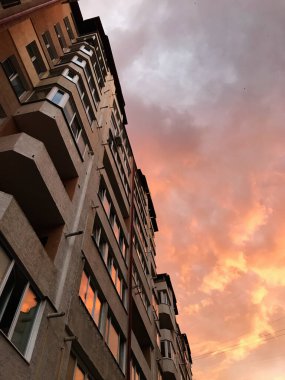 A low-angle view of a city building silhouetted against a stunning sunset sky with dramatic clouds. The warm tones of the sunset create a sense of tranquility and beauty. clipart