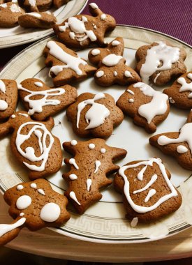 Beyaz kremayla süslenmiş ev yapımı zencefilli kurabiyelerden oluşan hoş bir düzenleme tabakta duruyor. Şenlikli şekiller Noel kutlamaları için mükemmel bir tatil ruhunu çağrıştırıyor..