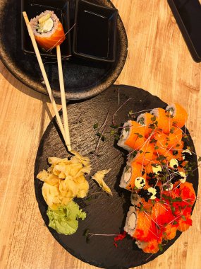 Soya sosu, zencefil ve kırsal bir masada wasabi ile servis edilen taze somon rulolarından oluşan güzel bir suşi tabağı. Mutfak konseptleri ve Japon mutfak temaları için ideal..