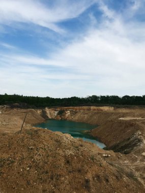 Bereketli yeşilliklerle çevrili parçalı bulutlu bir gökyüzünün altında turkuaz suyla dolu terk edilmiş bir taş ocağının sakin manzarası huzur ve doğaya bir kaçış sunuyor..