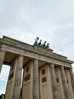 Berlin, Almanya 'daki etkileyici Brandenburg Kapısı, tarihi önemin ve mimari güzelliğin anıtsal bir sembolü, bulutlu bir gökyüzü arkaplanına karşı yakalandı..
