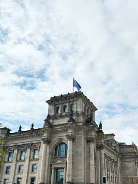 Parçalı bulutlu bir gökyüzüne karşı kurulmuş Avrupa bayrağı olan görkemli mimari yapı Reichstag binası. Süslü taş cephesi tarihi önemi ve kültürel mirası tasvir ediyor..