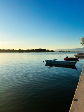 Akşamki sahnede sakin bir körfezin üzerinde demirli teknelerle sakin bir günbatımı resmediliyor. Durgun sular ve uzak ufuk sakin bir atmosfer yaratır, rahatlama ve yansıma için mükemmeldir. Nin, Hırvatistan.
