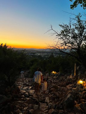 A family descends a rocky trail during a stunning sunset, capturing the essence of bonding and adventure. The scenic backdrop reveals a sprawling city illuminated by the warm evening glow. clipart