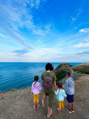 Dört kişilik bir aile uçurumdan nefes kesici bir okyanus manzarasının keyfini çıkarırlar. Mavi gökyüzü ve geniş manzara huzurlu ve maceralı bir atmosfer yaratıyor, unutulmaz bir gezi için mükemmel..