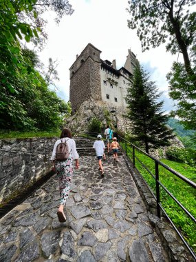 Bir grup turist, yemyeşil yemyeşil ile çevrili tarihi bir şatoya doğru pitoresk bir taş yolda yürüyor. Sahne keşif, macera, Bran, Romanya 'yı yansıtıyor.