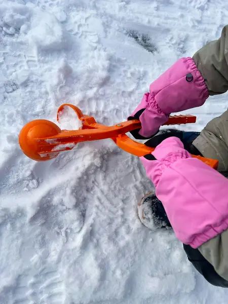 Taze karlı zeminde parlak bir turuncu kartopu makinesini kullanarak, kış aktivitelerini ve soğuk hava eğlencesini sergileyerek ellerinizi yakın plan yapın..