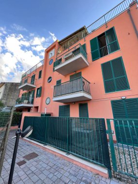 Parlak mavi gökyüzüne karşı yeşil panjurları ve balkonları olan canlı pembe bir apartman. Kentsel yaşam ve yaşam tarzı. Emlak ve mimari temalar için ideal.