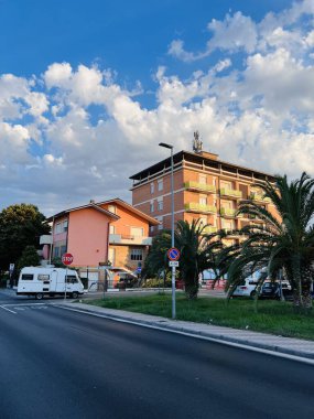 Açık mavi gökyüzünün altında canlı bir şehir. Palmiye ağaçları ve parlak bir apartman dairesi var. Arabalar sokağın yakınına park edilmiş sıcak ve rahat bir atmosfer sağlıyorlar..
