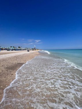 Berrak mavi bir gökyüzü ve kumlu sahilde dalgaların dalgalandığı sakin bir sahil sahnesi. Rahatlatıcı bir tatil ya da huzurlu sahil inzivaları hayalleri için mükemmel. Porto Sant 'Elpidio, İtalya.