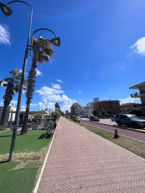 Açık mavi gökyüzünün altında palmiye ağaçları ve sokak lambalarıyla dolu güzel bir sahil geçidi. Kuruluş, kıyı kasabalarında rahatlama ve rahatlama hissi uyandırıyor. Porto Sant 'Elpidio, İtalya.