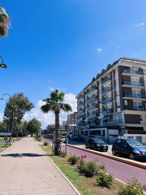 Porto Sant 'Elpidio, İtalya - 06 Temmuz 2022: Açık mavi gökyüzüne karşı palmiye ağaçları ve modern dairelerle kaplı bir yaya yolunun yer aldığı şehir manzarası. 