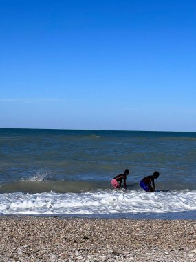 İki çocuk, açık mavi bir gökyüzünün altında dalgalarda yüzen okyanus kıyısında neşeli bir günün tadını çıkarıyorlar. Sahne, yazın neşesini ve özgürlüğünü yakalar..