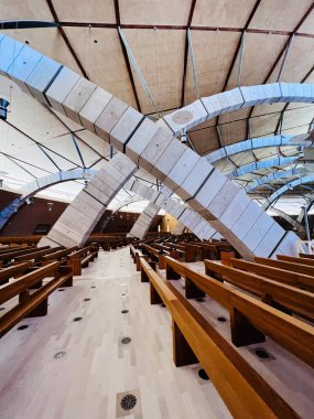 San Giovanni Rotondo, İtalya - 13 Temmuz 2022: Çarpıcı geometrik tavan mimarisi ve ahşap sıralar içeren çağdaş bir kilise iç mimarisi. 