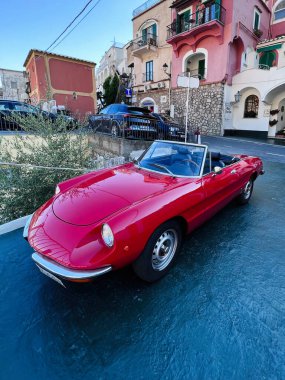 Positano, İtalya - 19 Temmuz 2022: Üstü açılabilir kırmızı bir Fiat arabası Avrupa 'nın pitoresk bir kasabasında park edilmiş, güzel mimari ve canlı renkler sergilenmektedir.. 