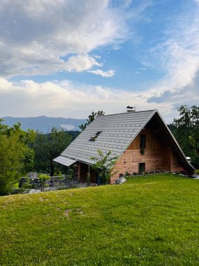 Parça bulutlu bir gökyüzünün altında güzel bir dağ manzarası olan yeşilliklerle çevrili ahşap bir kulübe. Huzurlu bir geri çekilme için mükemmel bir ortam..