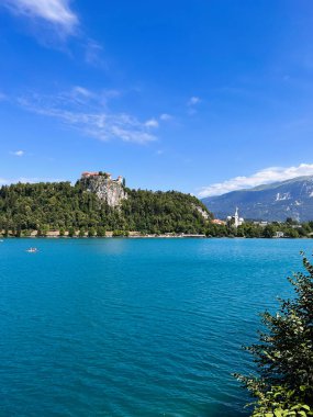 Berrak mavi gökyüzünün altında yemyeşil ve görkemli dağlarla çevrili tarihi bir şatosu olan sakin bir göl manzarası. Kan, Slovenya.