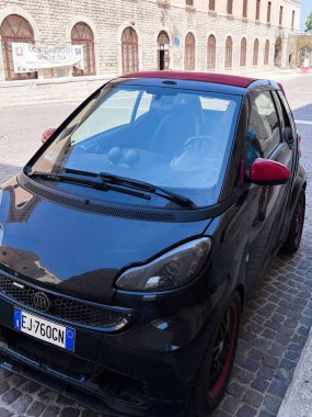 Bari, İtalya - 18 Temmuz 2022: Kırmızı aksanlı şık bir Brabus arabası güneşli bir kaldırım taşı caddesinde park edilmiştir. Arkaplanda tarihi bir taş bina yer alıyor ve kent sahnesine cazibe katıyor..