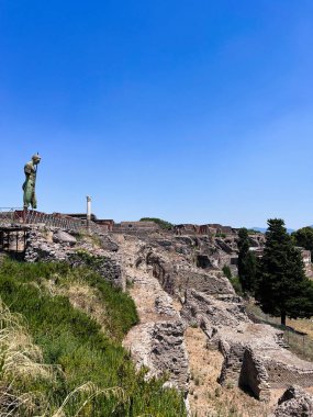 A scenic view of ancient ruins set against a vibrant blue sky, featuring a solitary statue in the foreground, evoking a sense of history and tranquility. Pompeii, Italy. clipart