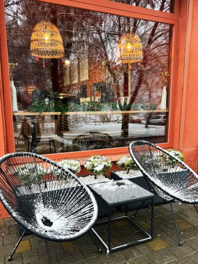 A charming cafe exterior featuring snow-covered chairs, wintertime ambiance, and seasonal holiday decorations showcasing a warm and inviting atmosphere. clipart