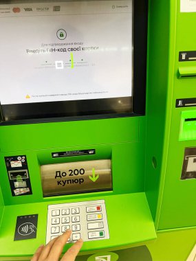 Kyiv, Ukrayna - 15 Aralık 2024: Bankacılık özelliklerine güvenli bir şekilde erişmek için PIN kodunu girerek ATM makinesini kullanan kişi. Yeşil arayüz ve tuş takımı görünür