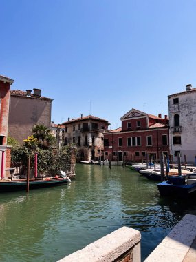 A picturesque view of a tranquil canal in Venice, Italy, surrounded by colorful buildings under a clear blue sky, capturing the essence of Venetian charm and serenity. clipart