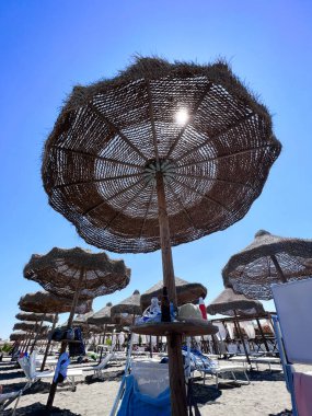 View of straw beach umbrellas under a clear blue sky on a sunny day. Perfect setting for relaxation and enjoying a beach holiday. Manfredonia, Italy. clipart