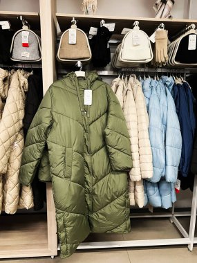 Kyiv, Ukraine - December 18, 2024: A green quilted winter coat hangs among other puffer jackets in beige and blue hues, part of a retail display with accessories like gloves and hats, showcasing fashionable seasonal wear. clipart