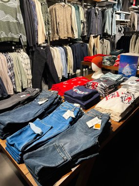 Kyiv, Ukrayna - 18 Aralık 2024: Katlanmış kot pantolonlar, mevsimlik kazaklar ve ahşap masalarda asılı gömlekler ve dış giysilerle çevrili aksesuarların yer aldığı mağaza içi perakendecisi, modaya uygun ve organize bir alışveriş uzmanının yakalanması