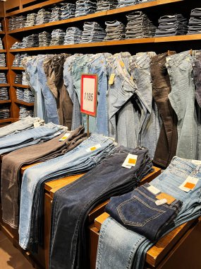 Kyiv, Ukrayna - 18 Aralık 2024: Bir perakende giyim mağazasında düzgünce sergilenen çeşitli katlanmış kot ve kot pantolon ürünlerine bakmak, alışveriş yapanlar için farklı stil, boyut ve tonları göstermek. Kurulum, organize ticaret ve ürün çeşitliliğini vurguluyor