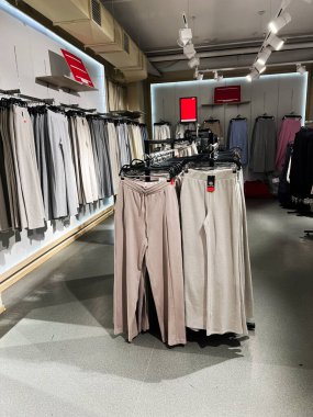 Kyiv, Ukraine - December 18, 2024: Interior of a clothing store featuring beige pants arranged on racks under stylish lighting, showcasing modern fashion. clipart