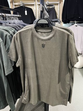 Kyiv, Ukrayna - 18 Aralık 2024: Basit ve pratik modanın vurgulandığı günlük kıyafet mağazasında küçük logolu bir zeytin yeşili tişört. Çekim vitrinleri bir alışveriş ortamında benzer giysi rafları düzenledi..