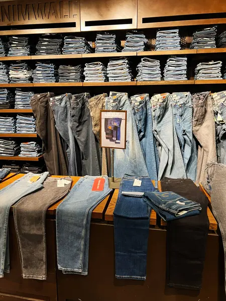 Kyiv, Ukrayna - 18 Aralık 2024: Bir perakende giyim mağazasında çeşitli kot pantolonlar sergileniyor, raflar ve masalarda farklı stil ve renkler sergileniyor. Müşteriler için günlük giyim seçeneklerini ve moda eğilimlerini vurgular. 