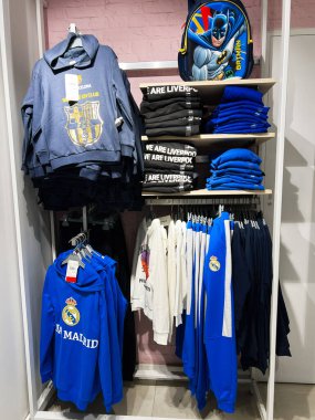 Kyiv, Ukrayna - 18 Aralık 2024: Çeşitli markalı kapüşonlular ve spor temalı kıyafetler bir perakende mağazasının raflarında düzgünce sergileniyor. Özelleştirilen eşyalar arasında popüler futbol takımı malları ve temalı sırt çantaları, güçlü spor ve pop kültürünün kullanılması yer alıyor.