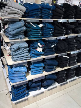 Kyiv, Ukrayna - 18 Aralık 2024: Düzenli bir perakende mağazası rafı farklı stil ve renkte kot düzgünce sergilenmiş ve istiflenmiş. Düzenli ve profesyonel bir alışveriş ortamı sunuyor. Çeşitli kot kıyafetleri sergileniyor.. 