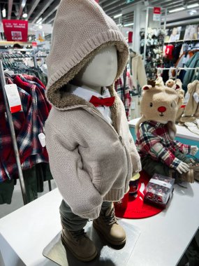 Kyiv, Ukraine - December 18, 2024: Mannequin showcasing a stylish child's winter outfit with knitted hoodie, boots, and red bowtie in a retail shop's festive-themed showcase featuring holiday decorations and cozy clothing.  clipart