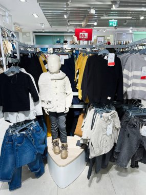 Kyiv, Ukraine - December 18, 2024: A retail store displays a collection of children's clothing on racks, with a mannequin showcasing an outfit. The store is bright and modern with visible sale signage promoting discounts. clipart