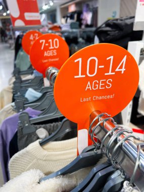 Kyiv, Ukraine - December 18, 2024: Close-up of a children's clothing rack featuring size labels and garments in a retail store. The organized display emphasizes age ranges with bright signage, offering a clear shopping experience for customers. clipart