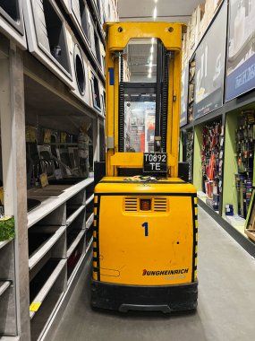 Kyiv, Ukraine - January 03, 2025: A yellow forklift placed in the aisle of a hardware store surrounded by shelves. The forklift is compact and used for handling inventory within the store. Various tools and items line the shelves. clipart